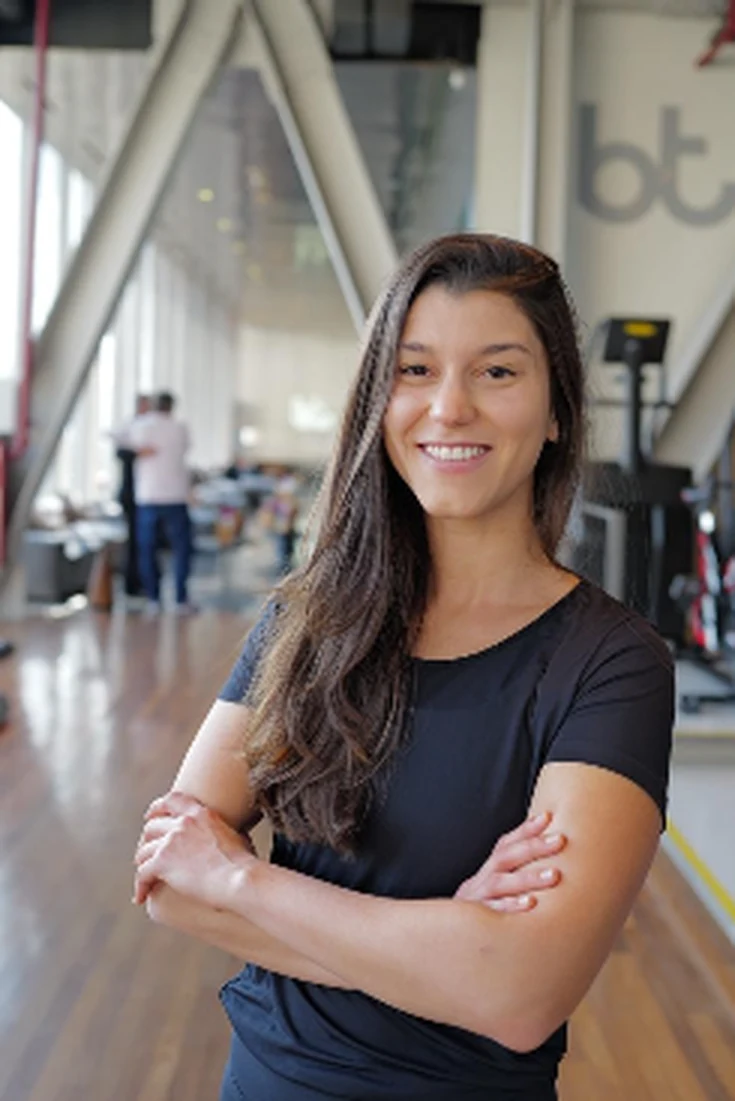 Maria Camila sorrindo na academia, com os braços cruzados